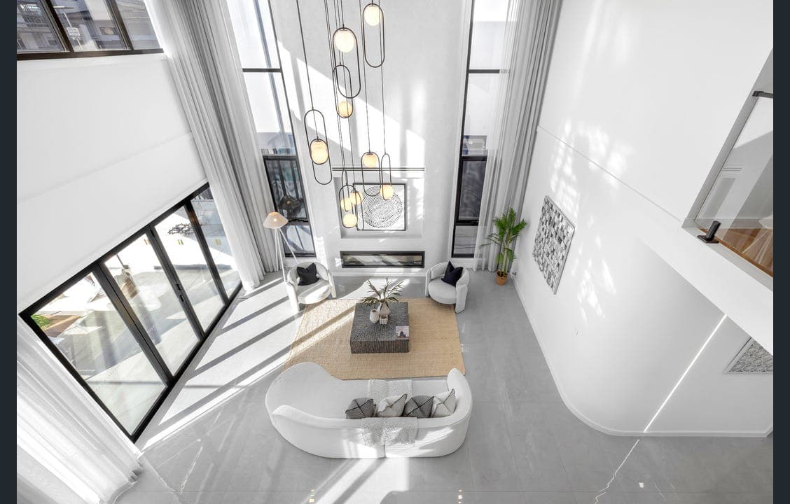 Double-height living room styled by RitZi Stagings with a sculptural pendant light and curved white sofa, seen from the mezzanine above.
